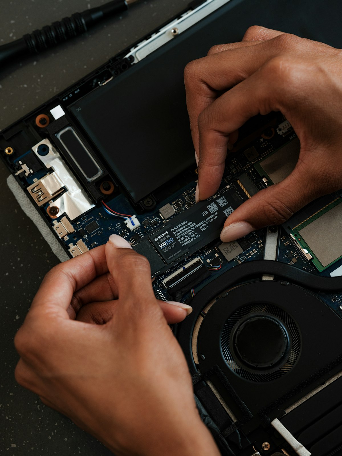 Technician working on a laptop motherboard near the charging ports