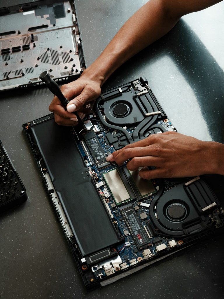 Laptop opened on a repair bench while a technician works on it